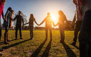 Gruppe junger Menschen hält sich bei Sonnenaufgang im Kreis an den Händen